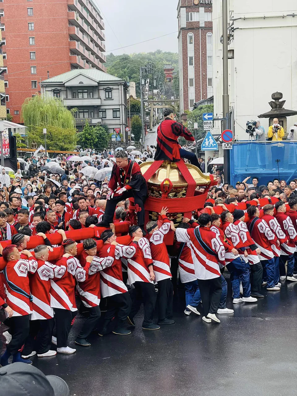 La procession du mikoshi du festival d’automne de Dōgo sous la pluie, avec les équipes en kimono rouge et blanc avançant dans les rues de Matsuyama.