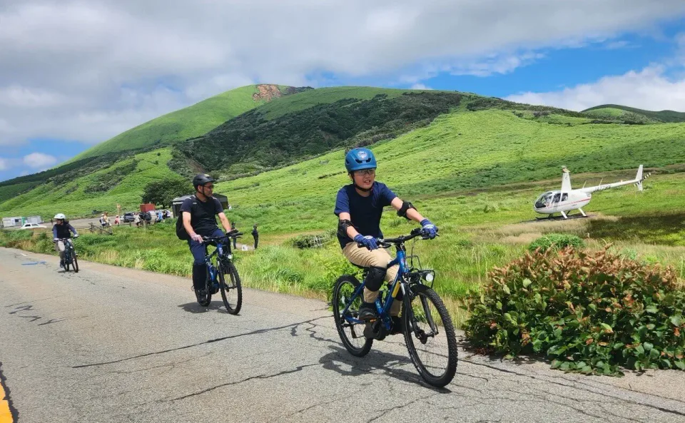 Cyclists riding e-bikes through the volcanic grasslands of Aso