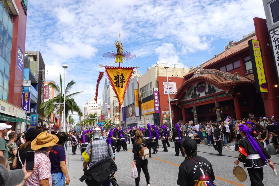 ขบวนแห่ธงใหญ่ของนาฮะเคลื่อนผ่านถนนคานาซาวะ โดยมีธงและขบวนแห่แบบดั้งเดิมรวมตัวกัน