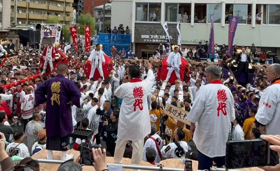 Sur le site du rassemblement du Matsuyama Autumn Festival, deux mikoshi (palanquins divins) s’approchent, entourés de porteurs et de spectateurs très nombreux.