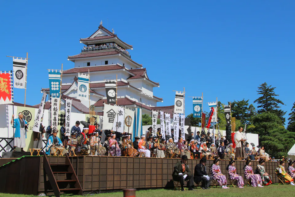 Le stand du festival d’Aizu devant le château de Tsuruga, avec les drapeaux des anciens seigneurs, reflète l’atmosphère historique du festival d’Aizu.