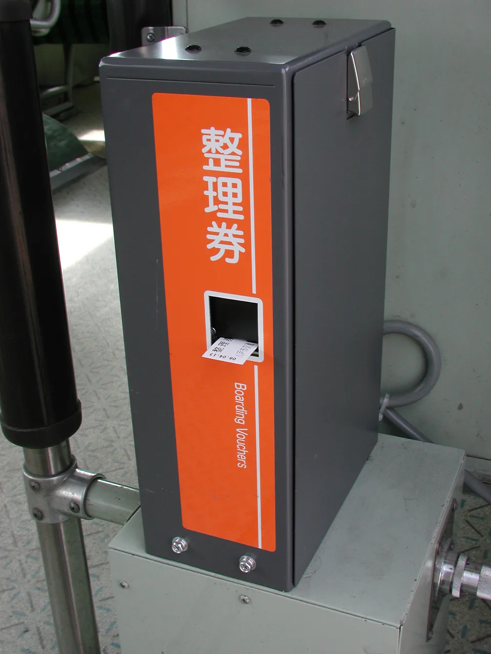 A numbered-ticket dispenser beside the boarding door of a Japanese regional bus