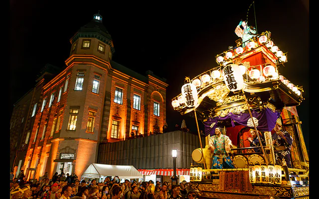 Scène réelle du festival de Kawagoe après la tombée de la nuit, avec les yatai illuminés et la musique traditionnelle