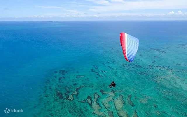 沖繩動力滑翔傘在珊瑚礁海面上空飛行；實際空中時間應與商品總時數分開比較。